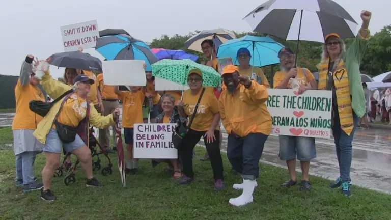 Several UU members smiling and posing near the side of the street in the rain with umbrellas and anti-ICE signs.